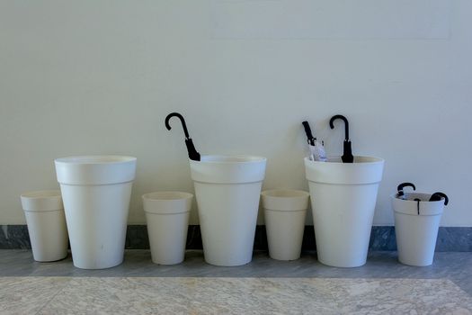 A minimalist display featuring white containers holding black umbrellas, set indoors.
