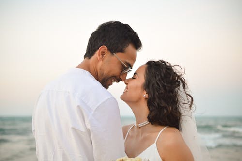 A bride and groom are standing on the beach