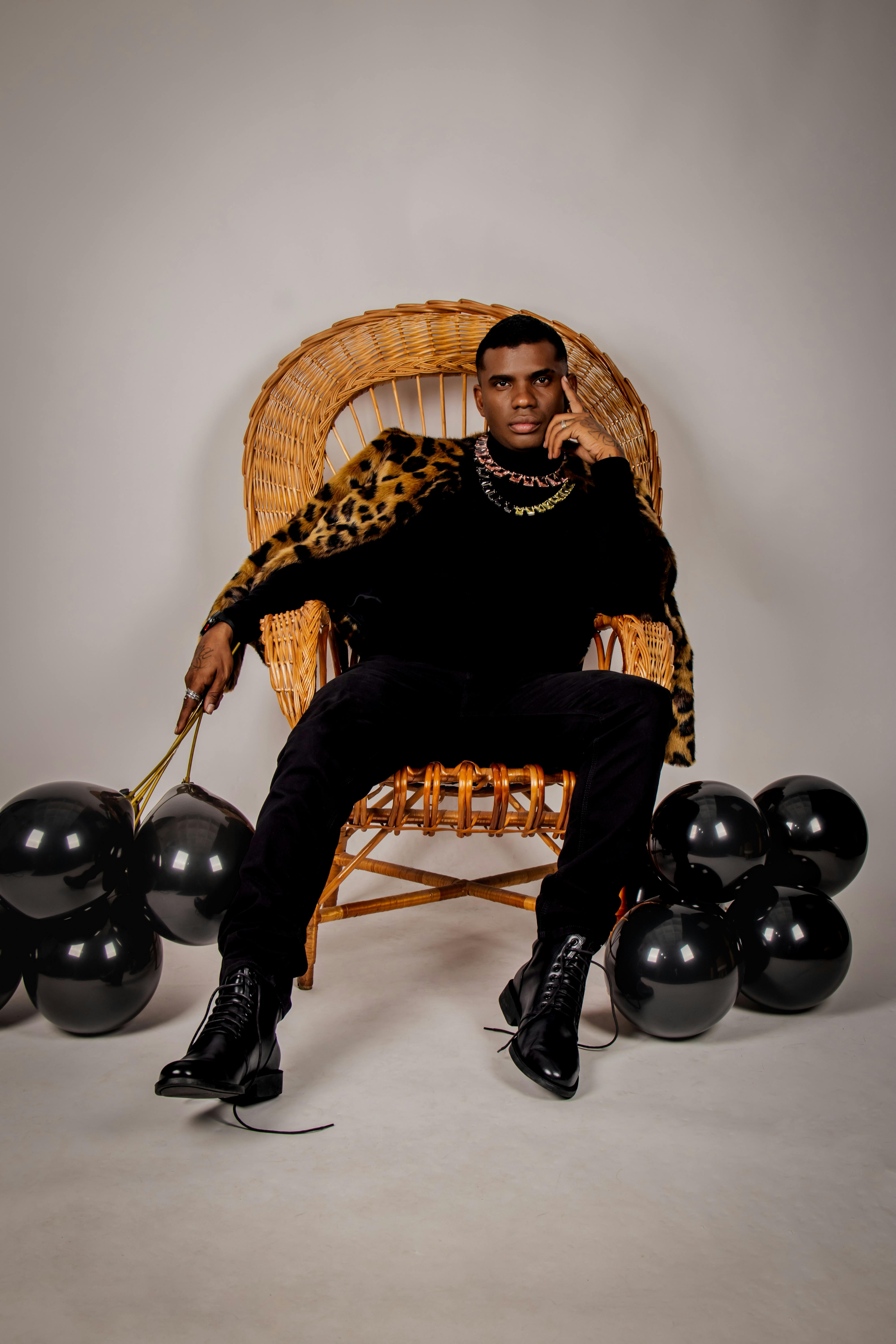 Elegant studio shot of a man in a leopard coat, black balloons, and leather boots.