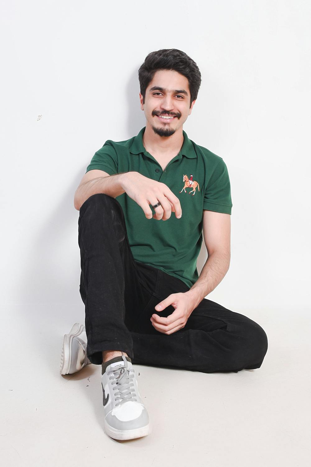 Young Man Smiling Sitting Wearing Green Polo Shirt and Black Trousers