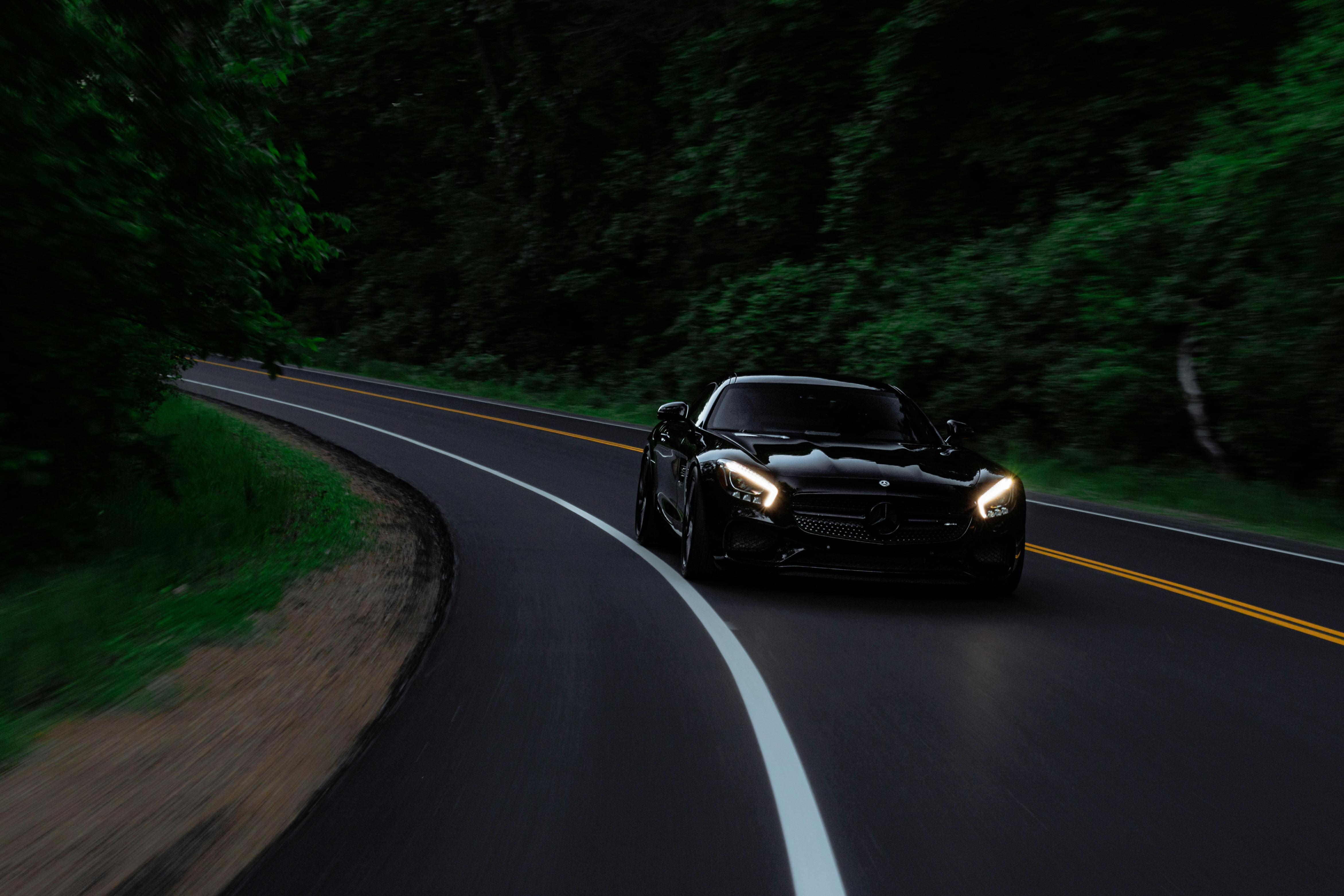 Black sports car driving through a winding forest road, headlights illuminating the path