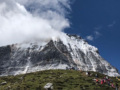 Snow-capped mountain with climbers and lush greenery under a bright blue sky.
