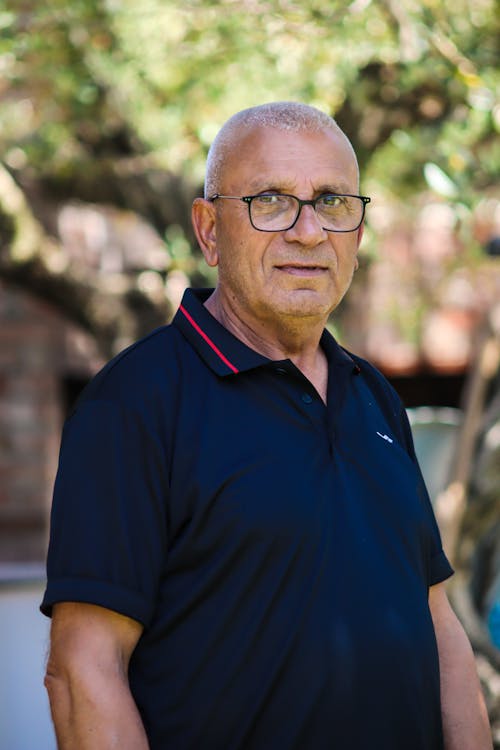 A man in a black shirt and glasses standing in front of trees