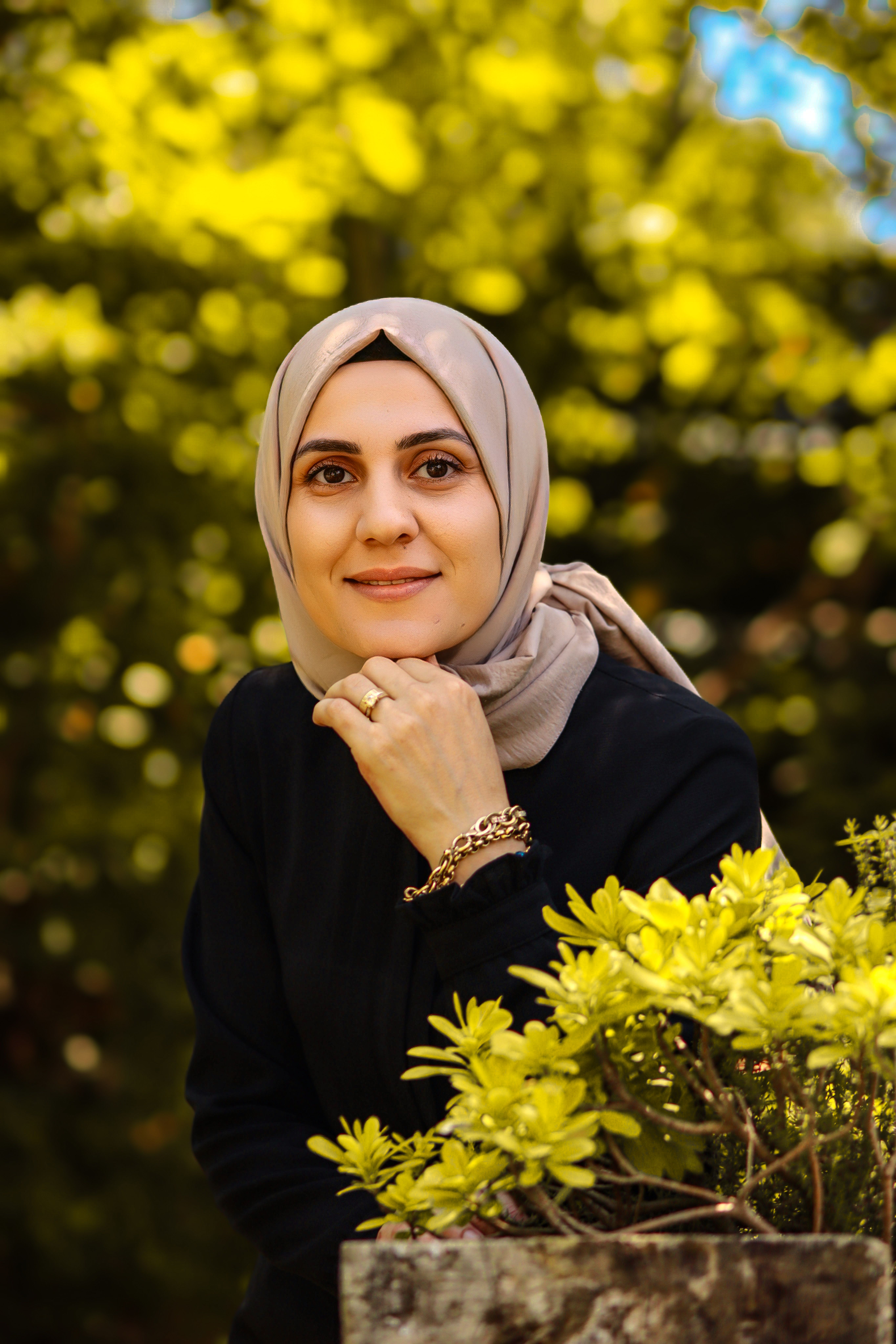 Smiling woman in a headscarf among vibrant green foliage outdoors.
