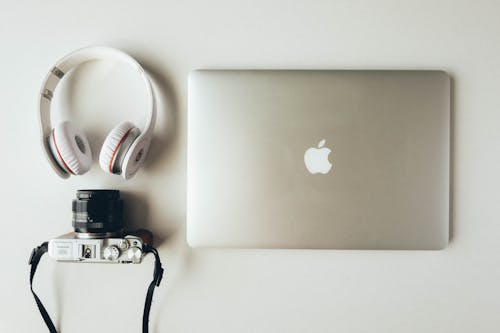 Silver Macbook Beside Headphones and Camera