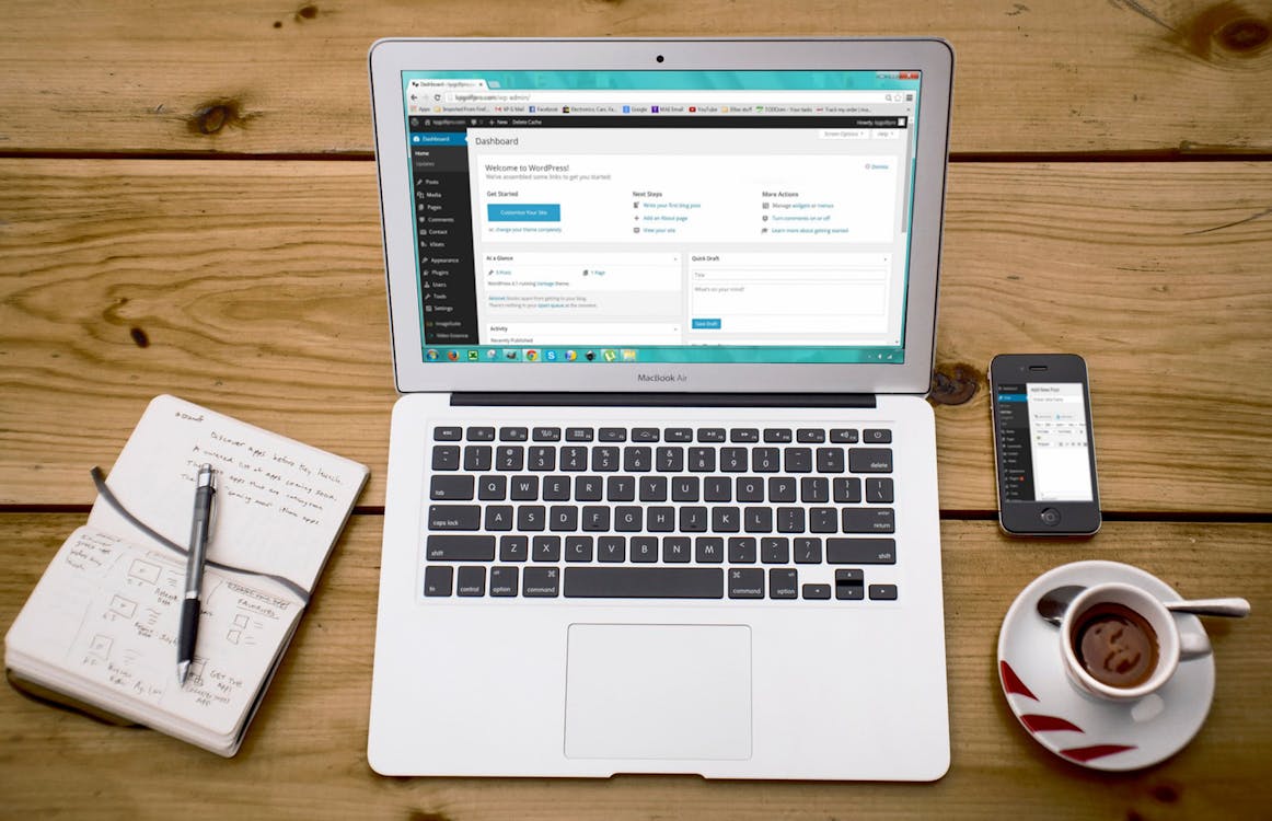 A laptop showing WordPress next to a mug of coffee, a notebook, and an iPhone. 