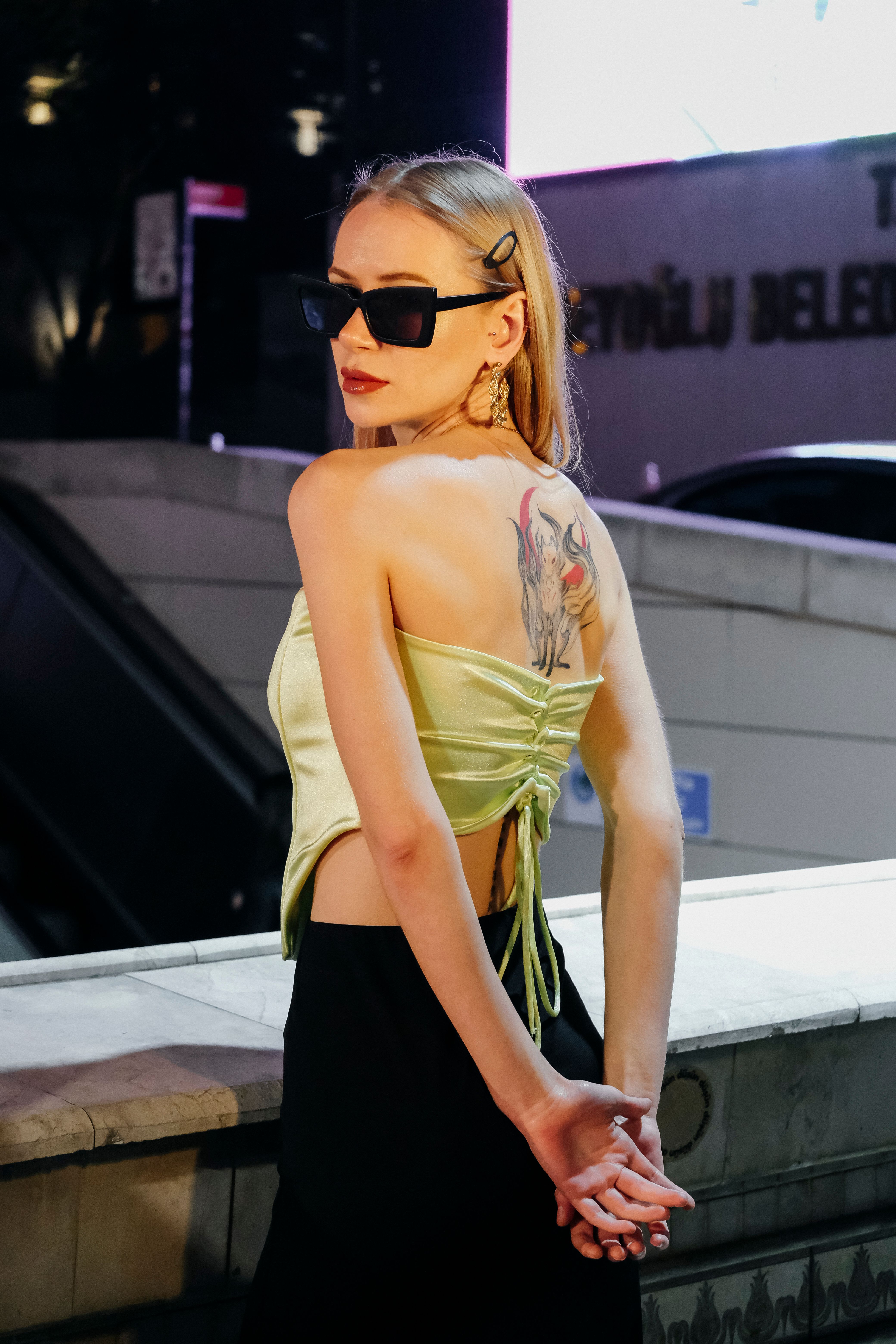 Fashionable woman posing with tattoo in urban night setting.
