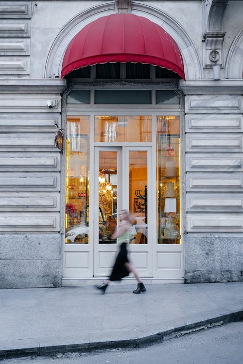 A woman walking past a store with a red awning