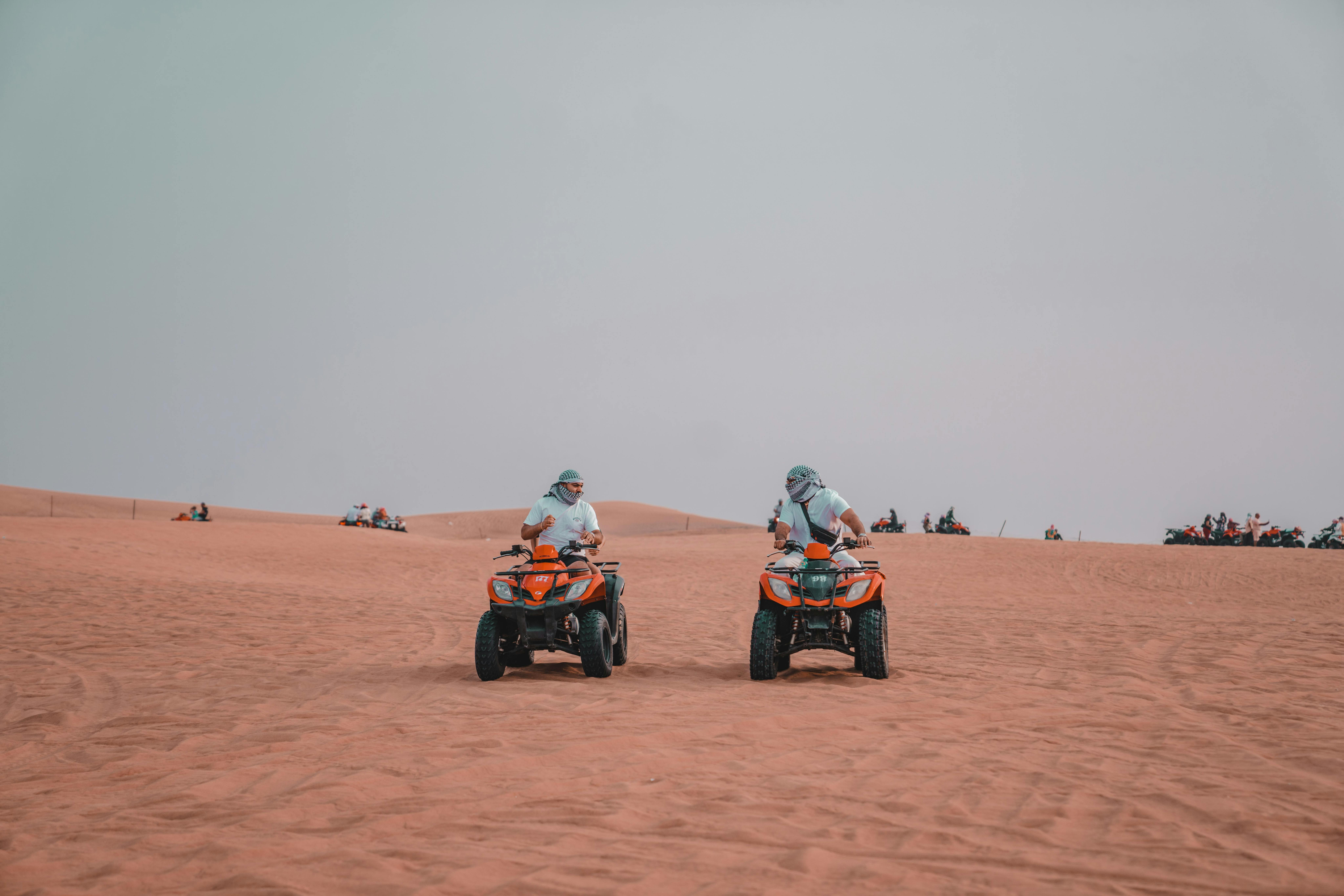 Two men riding ATVs on vast desert dunes, depicting an exciting outdoor adventure.