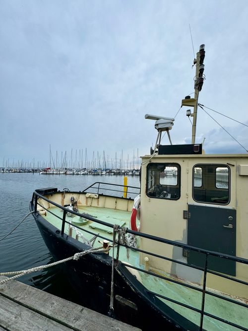 Free A fishing boat quietly moored in a peaceful harbor with a cloudy sky. Stock Photo