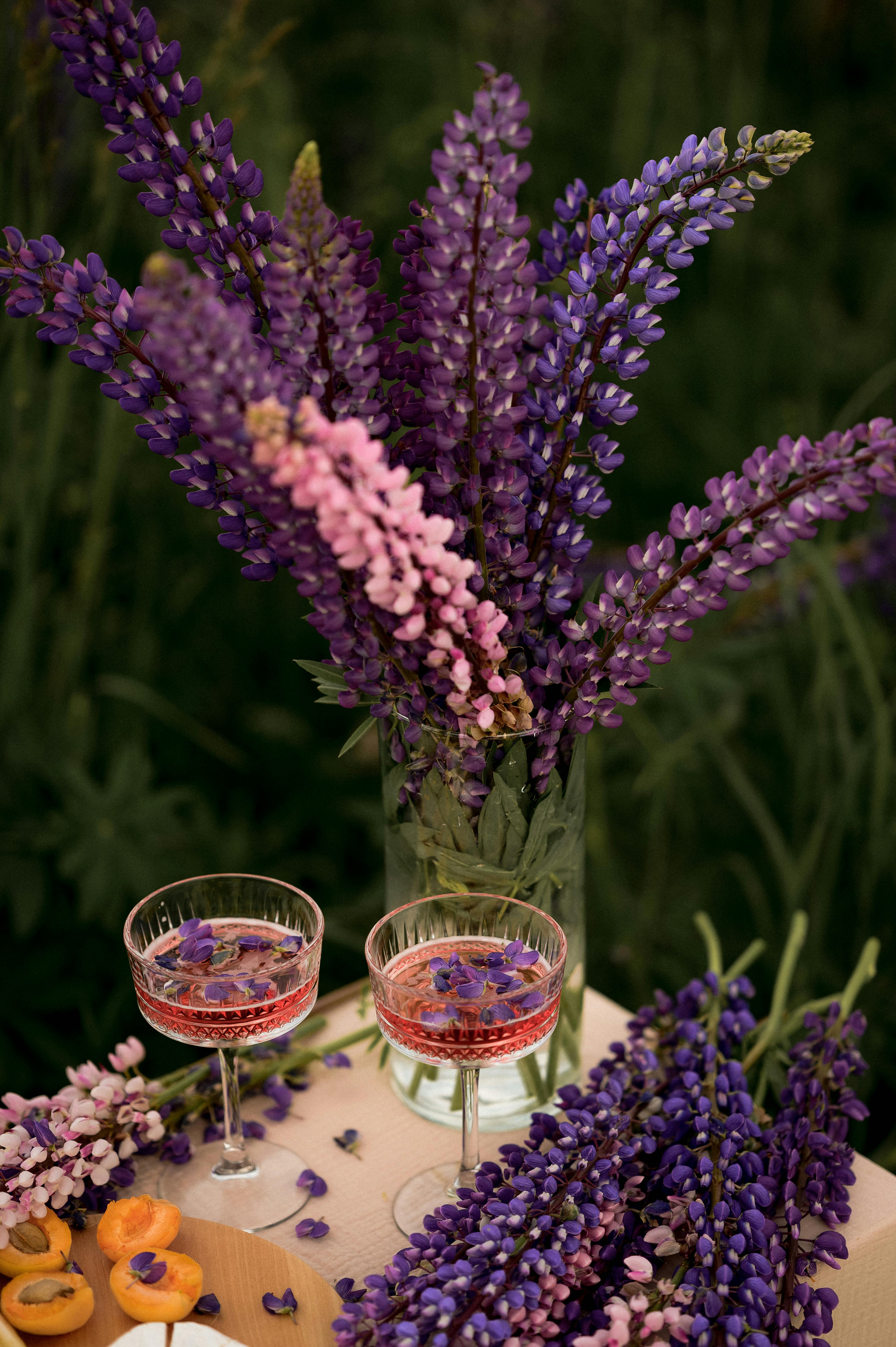 A beautiful arrangement of purple lupins in a vase by two elegant drinks, perfect for a summer garden setup.