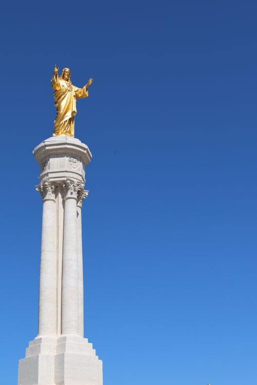 Free Golden statue of Jesus on a tall column against a clear blue sky, captured in Portugal. Stock Photo