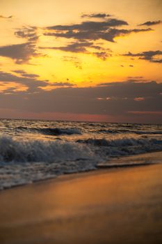 Vibrant sunset casting orange hues over gentle ocean waves on a sandy beach.