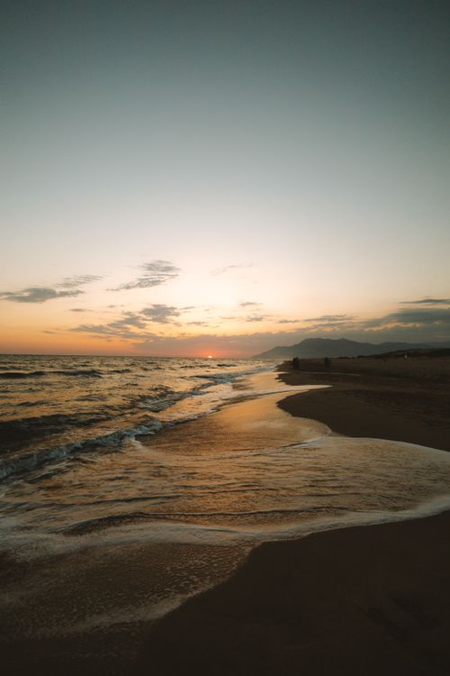 Free Peaceful beach sunset with vibrant colors and gentle waves reflecting on the shore. Stock Photo
