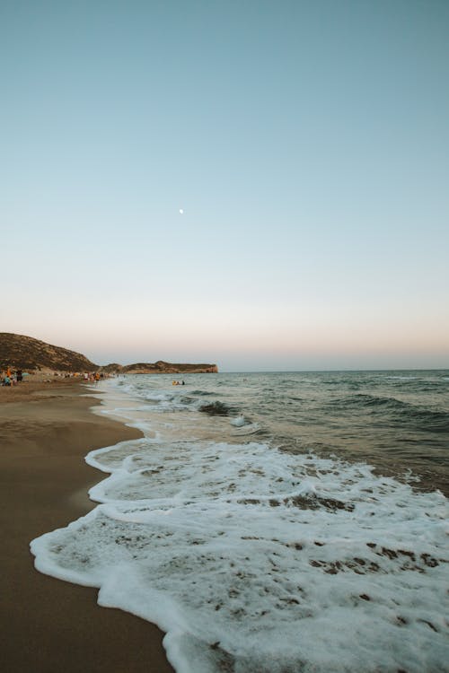 A beach with waves and the moon in the sky