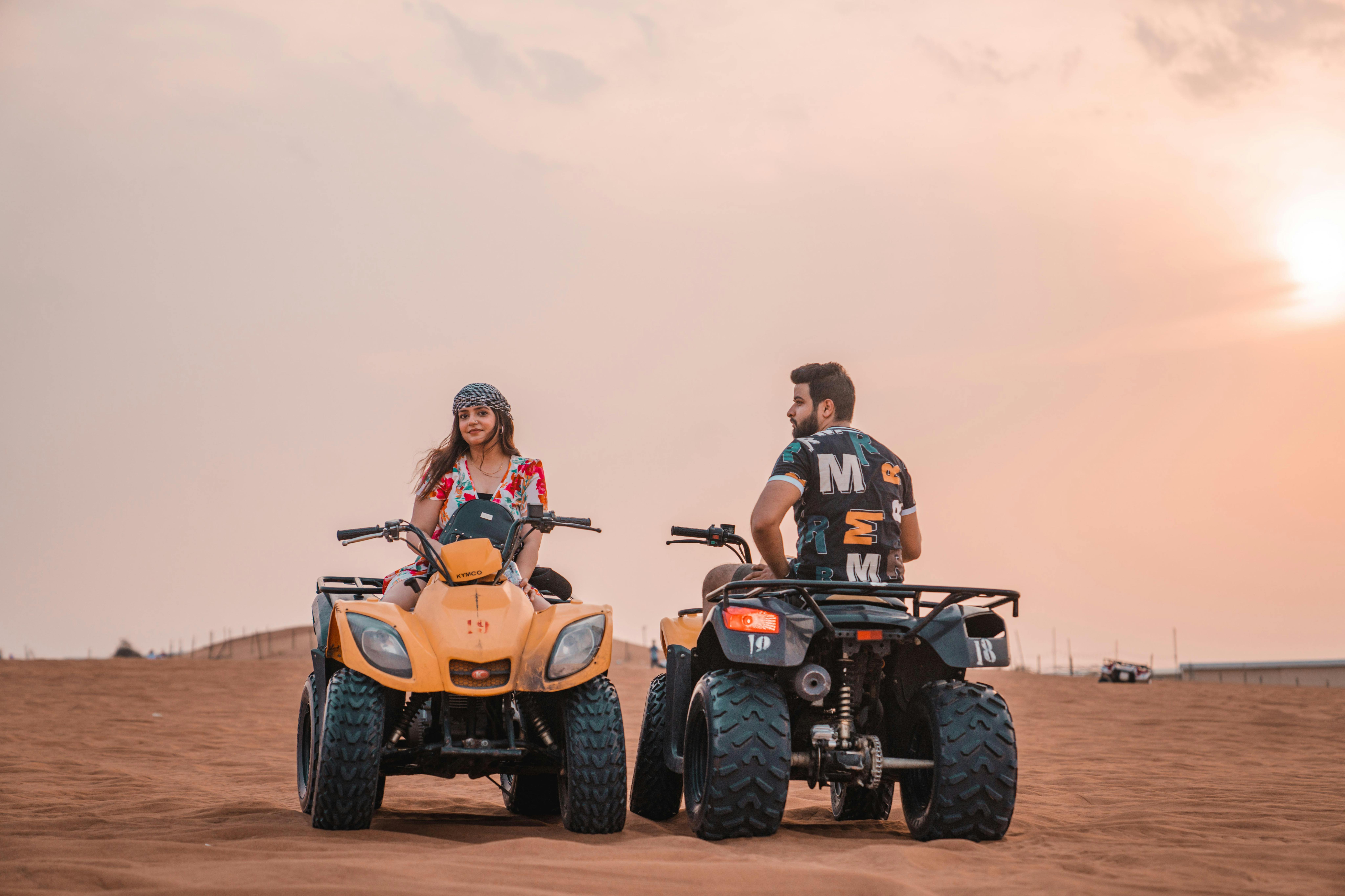 A couple enjoys a thrilling quad bike ride in the desert during a stunning sunset, evoking adventure
