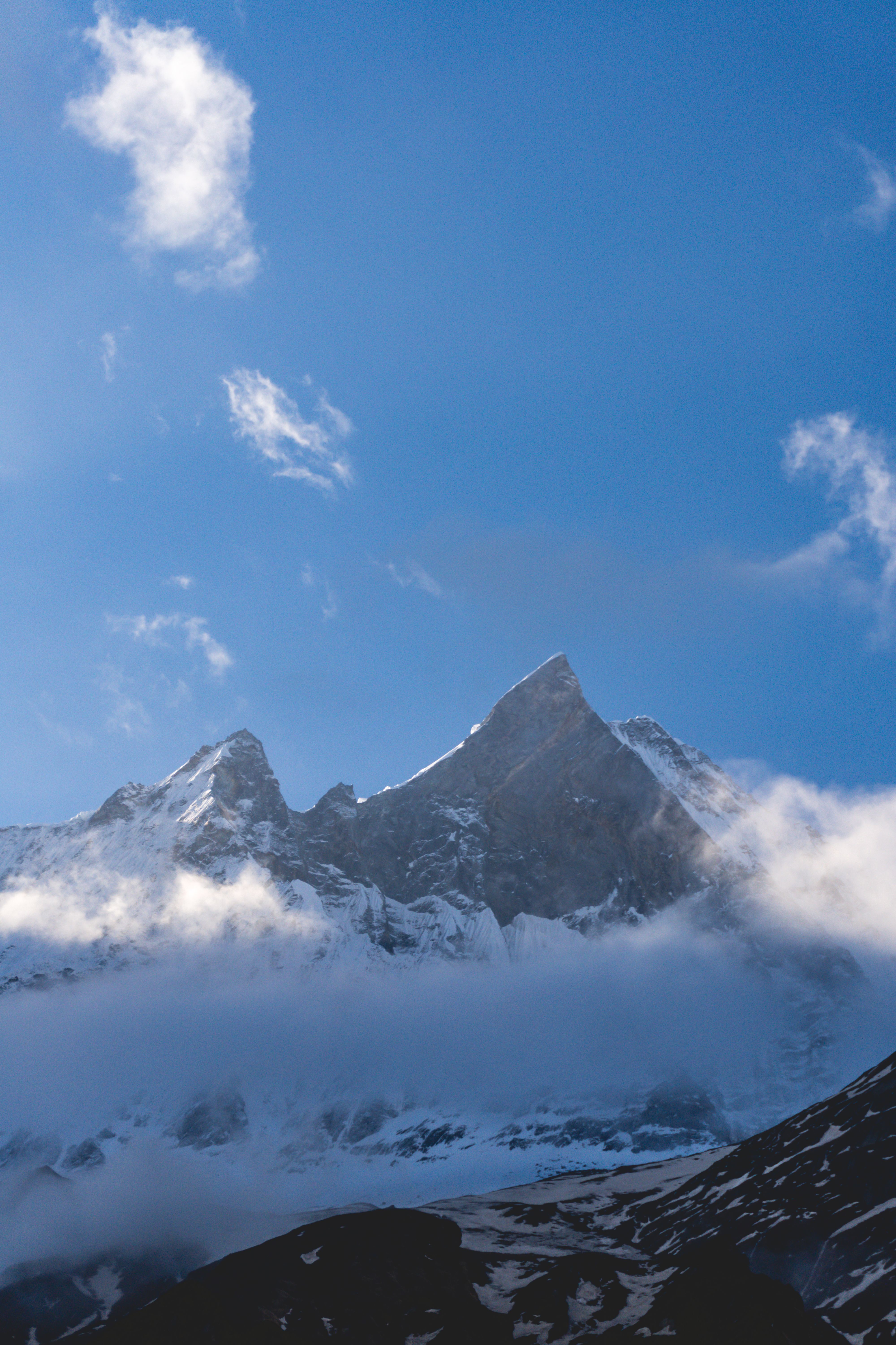 Capture of the majestic Machapuchare peak with clear blue skies and clouds in Gandaki Province, Nepal.