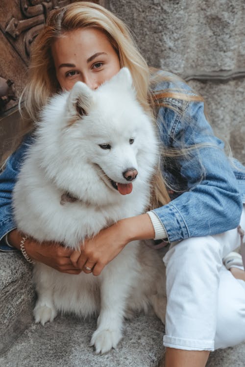 A woman in denim jacket hugging a white dog