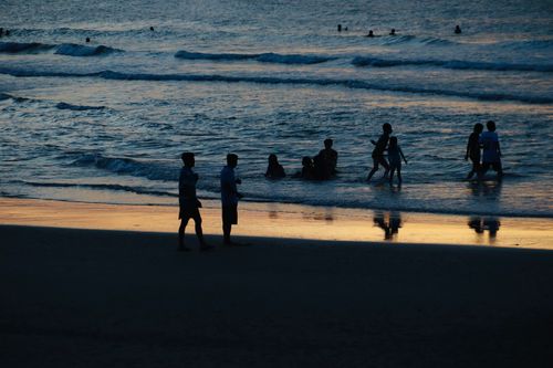 Free A serene beach scene with silhouettes of people enjoying the ocean at sunset. Stock Photo