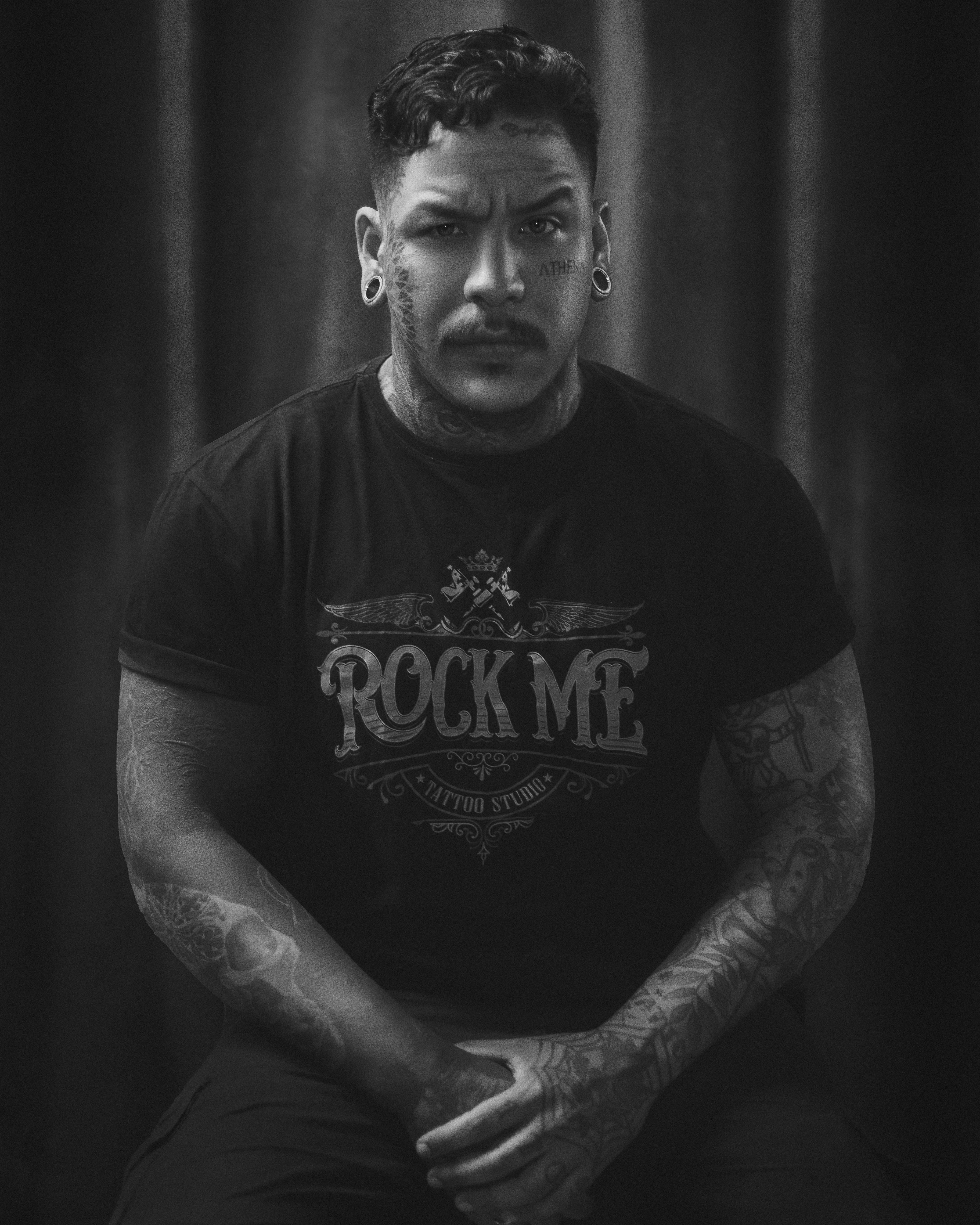 Dramatic black and white portrait of a tattooed male model sitting confidently.