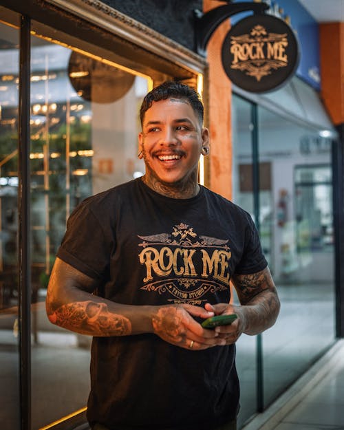 A man in a black shirt and tattoos standing outside a store