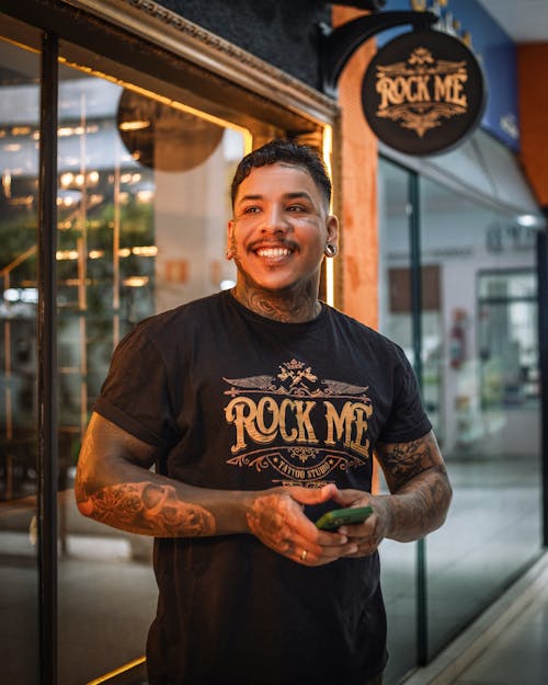 A man with tattoos standing in front of a rock me store