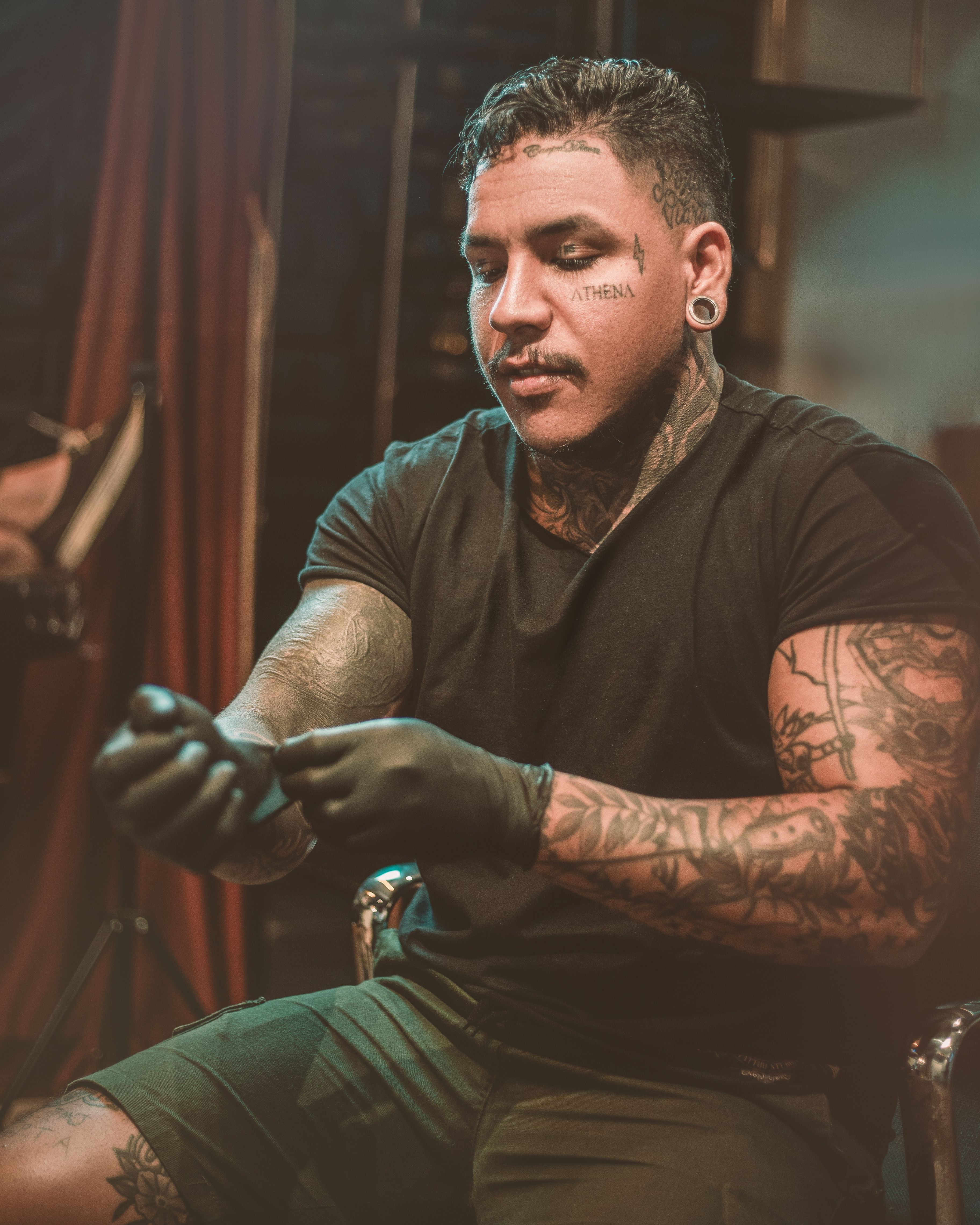Tattoo artist with gloves and tattoos prepares in studio. Warm mood lighting enhances the atmosphere.