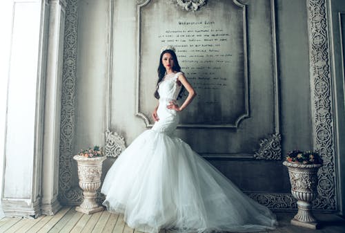 бесплатная Женщина в белом свадебном платье стоит у стены, окрашенной в серый цвет Стоковое фото