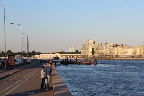 Free People stroll along a riverside promenade with cityscape views during a serene sunset. Stock Photo