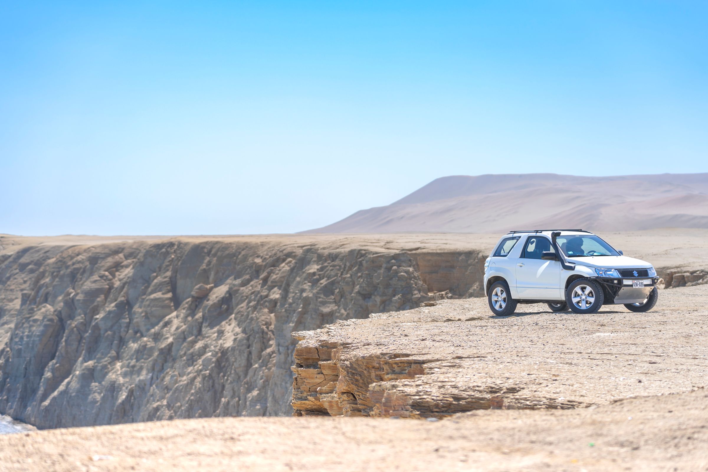 White SUV parked overlooking a vast desert landscape on a summer road trip