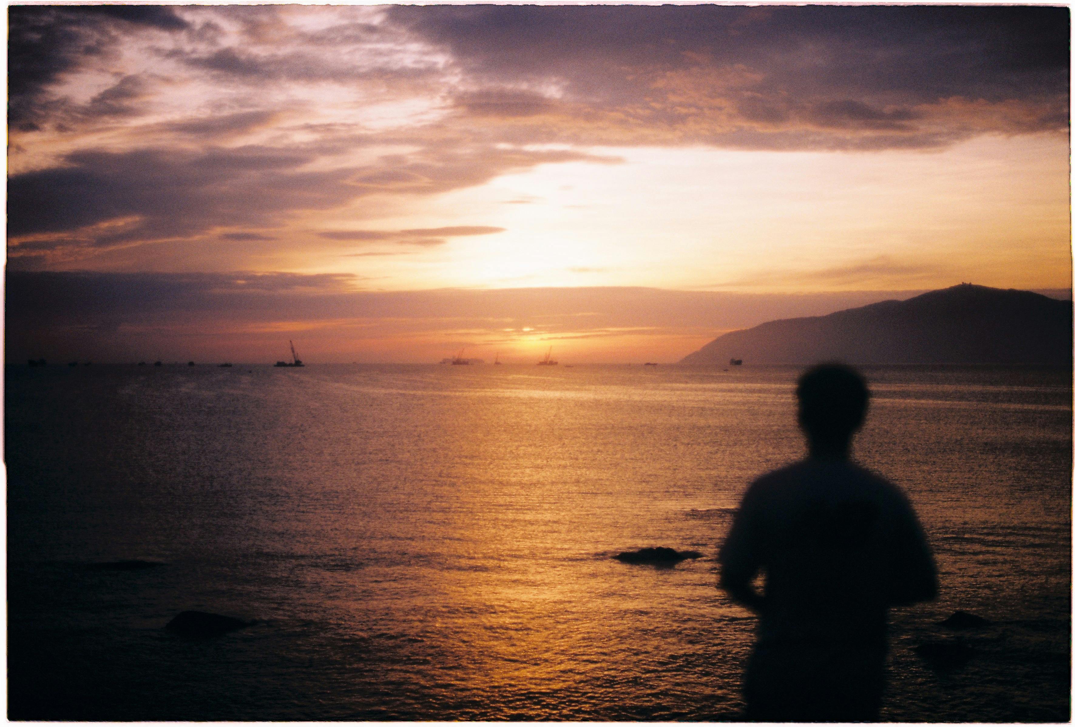 silhouette of man by the sea during sunset