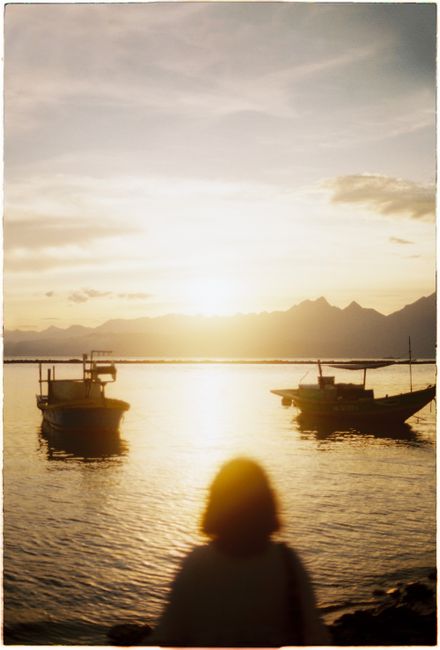 Silhouette of a woman gazing at boats on a tranquil lake during sunset in Da Nang, Vietnam.