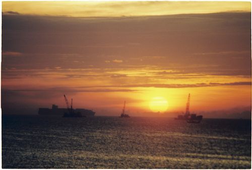 Free Tranquil sunset over Da Nang sea featuring silhouetted ships and cranes against a vivid horizon. Stock Photo