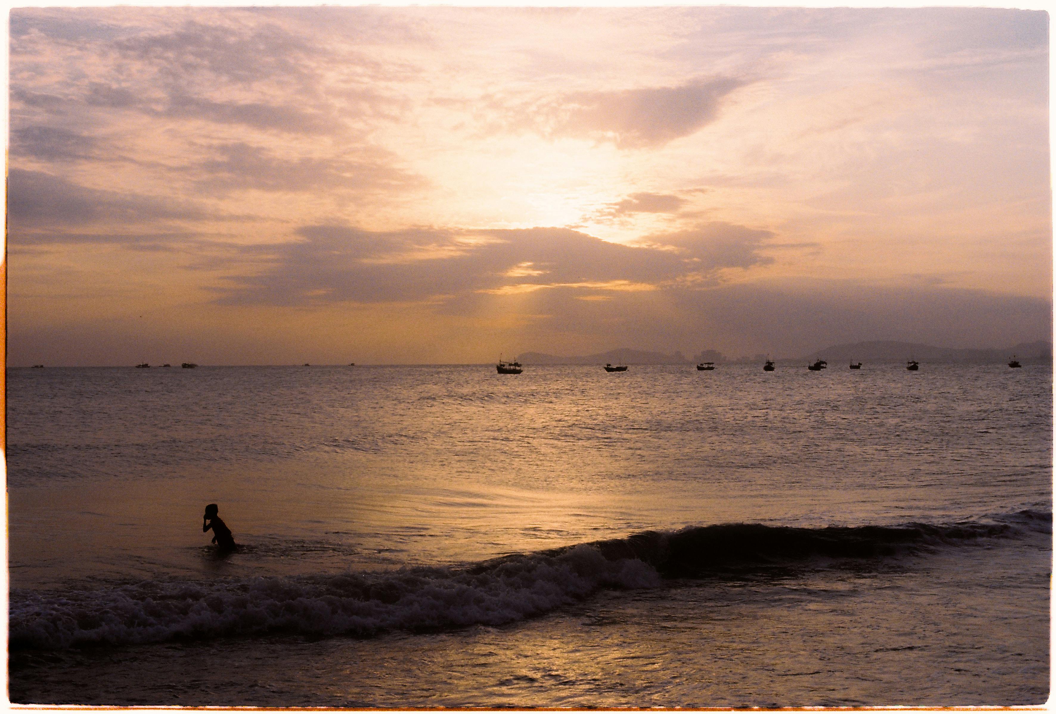 Serene view of a sunset over Vũng Tàu, Vietnam, featuring a lone silhouette and distant boats.