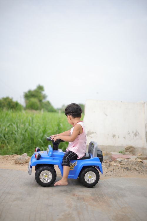 Free A young child having fun on a blue toy car in an outdoor setting. Perfect for childhood and outdoor play concepts. Stock Photo