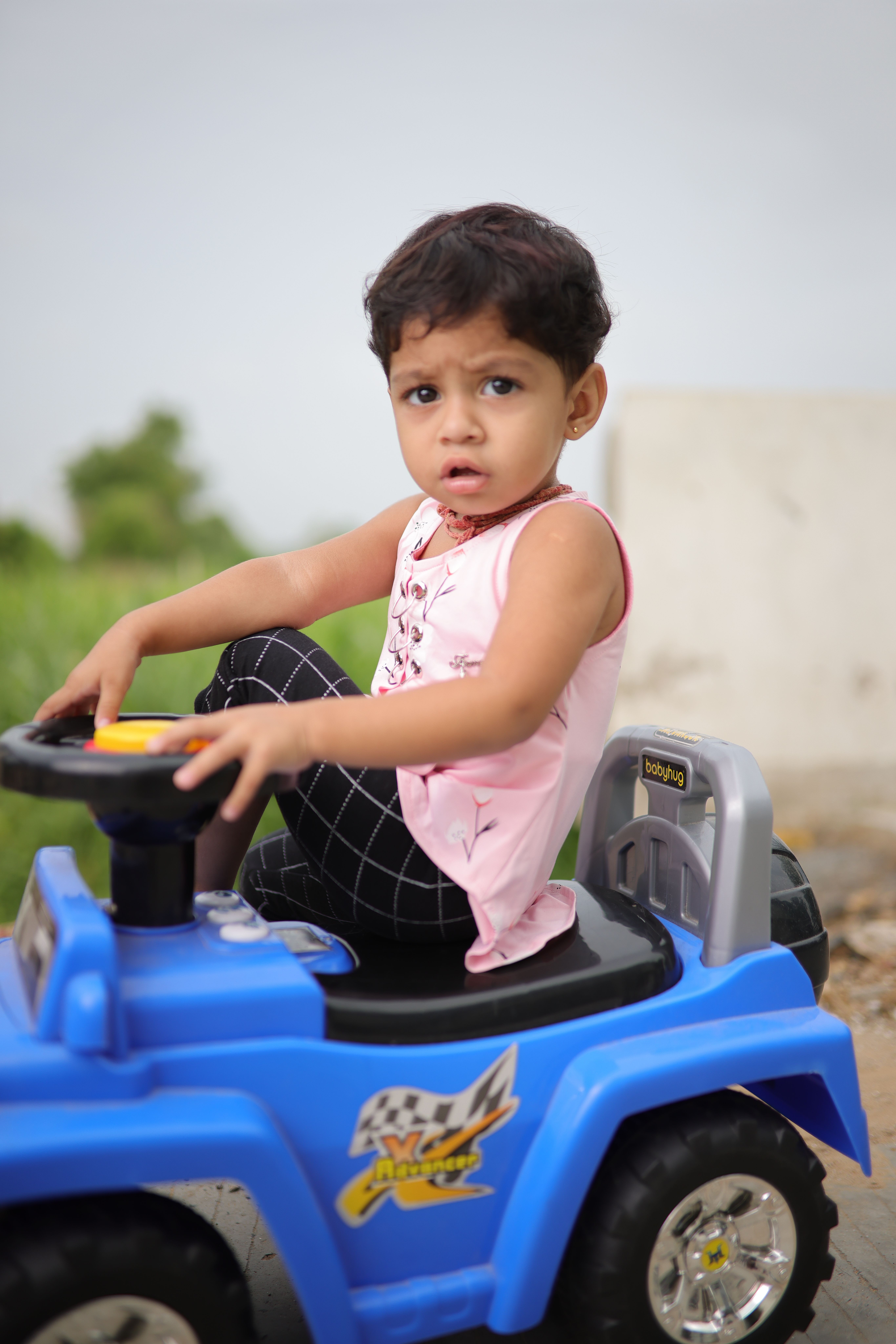 Young girl riding a blue toy car outdoors, showcasing fun and playfulness on a sunny day.