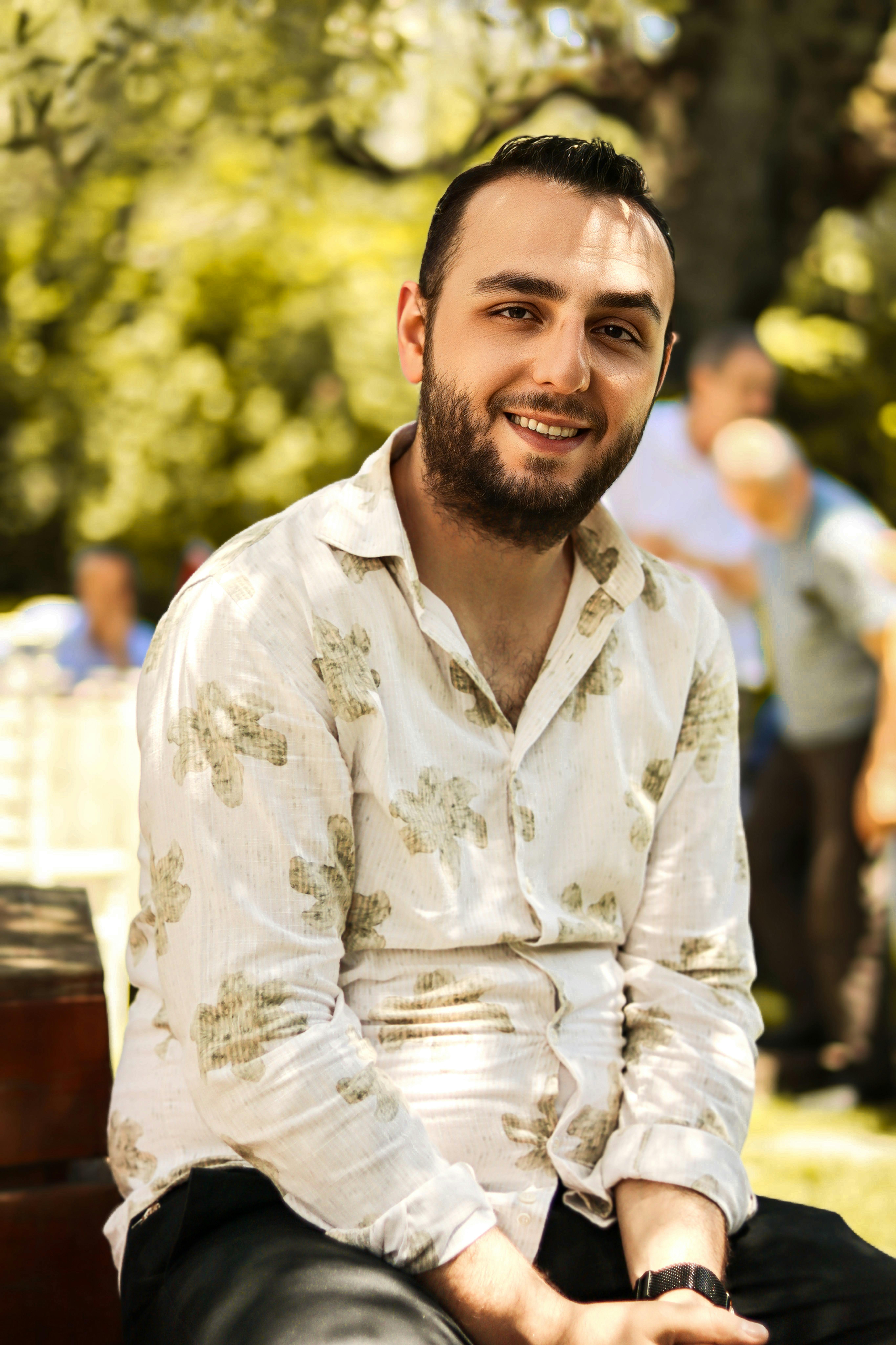 A casually dressed man with a beard enjoying a sunny day while sitting on a park bench.