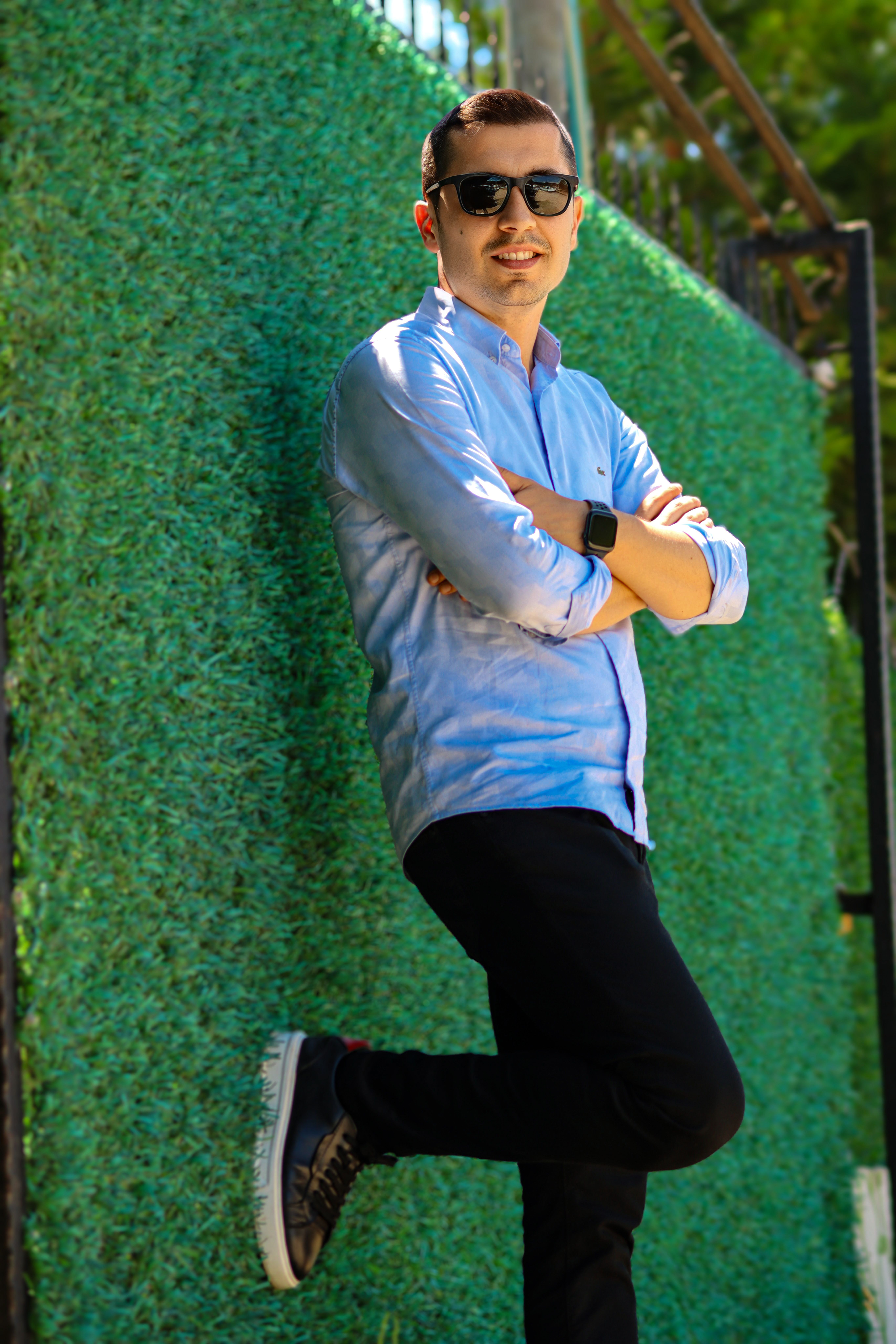 Fashionable man in sunglasses leaning on a vibrant green wall under summer sunlight.