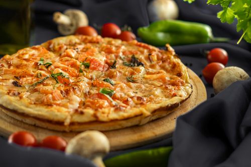 Free Mouthwatering pizza with fresh ingredients and vibrant vegetables around, perfect for food lovers. Stock Photo
