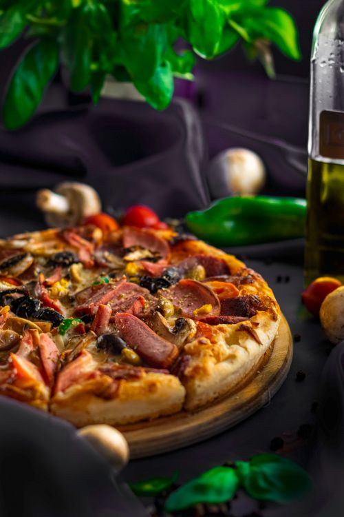 Free Mouth-watering pizza topped with meats and vegetables on a rustic setting. Stock Photo