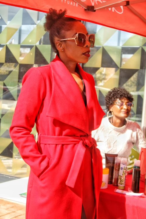 Free Woman in a red coat and sunglasses standing at an outdoor event with colorful patterns. Stock Photo