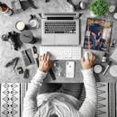 一张俯视视角下井然有序的办公桌，上面摆放着科技小工具、时尚杂志以及适合现代工作生活方式的配件