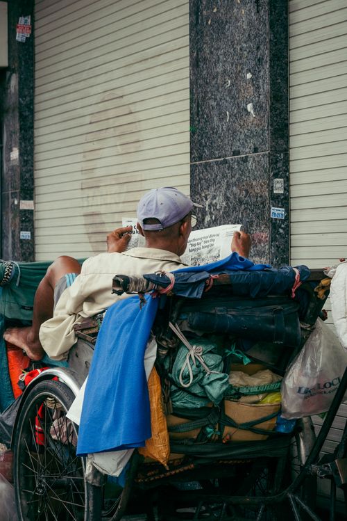 Free A person reading a newspaper while resting on their cart on a city street in Ho Chi Minh City. Stock Photo
