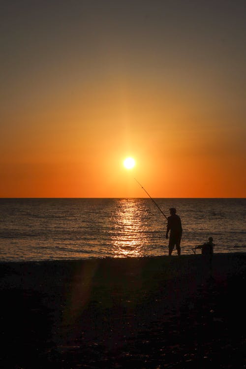 A man fishing at sunset on the beach