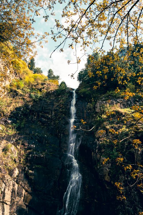 Free A breathtaking view of a waterfall flowing down a rugged cliff surrounded by autumn foliage. Stock Photo