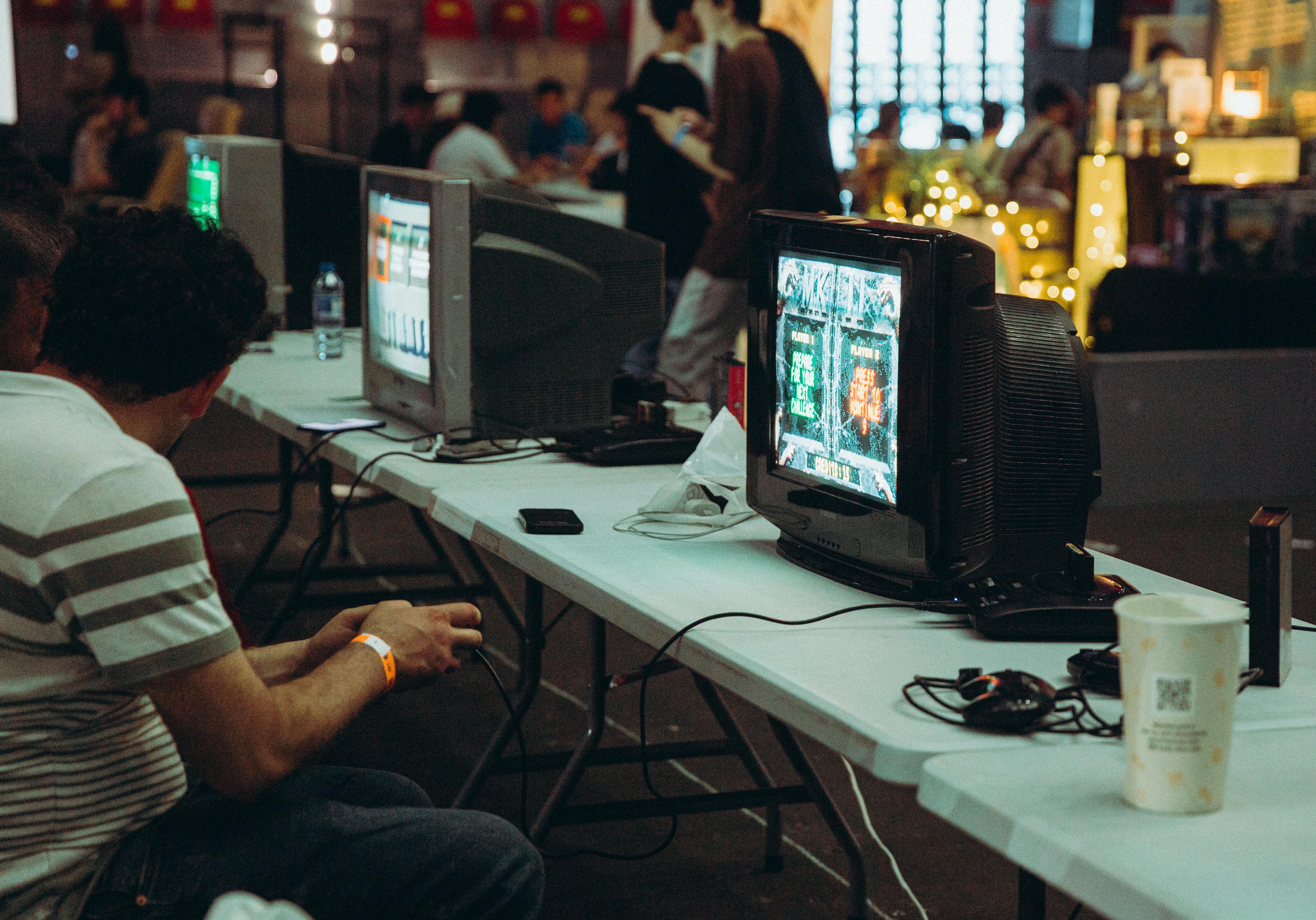 Adults enjoying a retro gaming event with CRT televisions and consoles, creating a nostalgic atmosphere indoors.