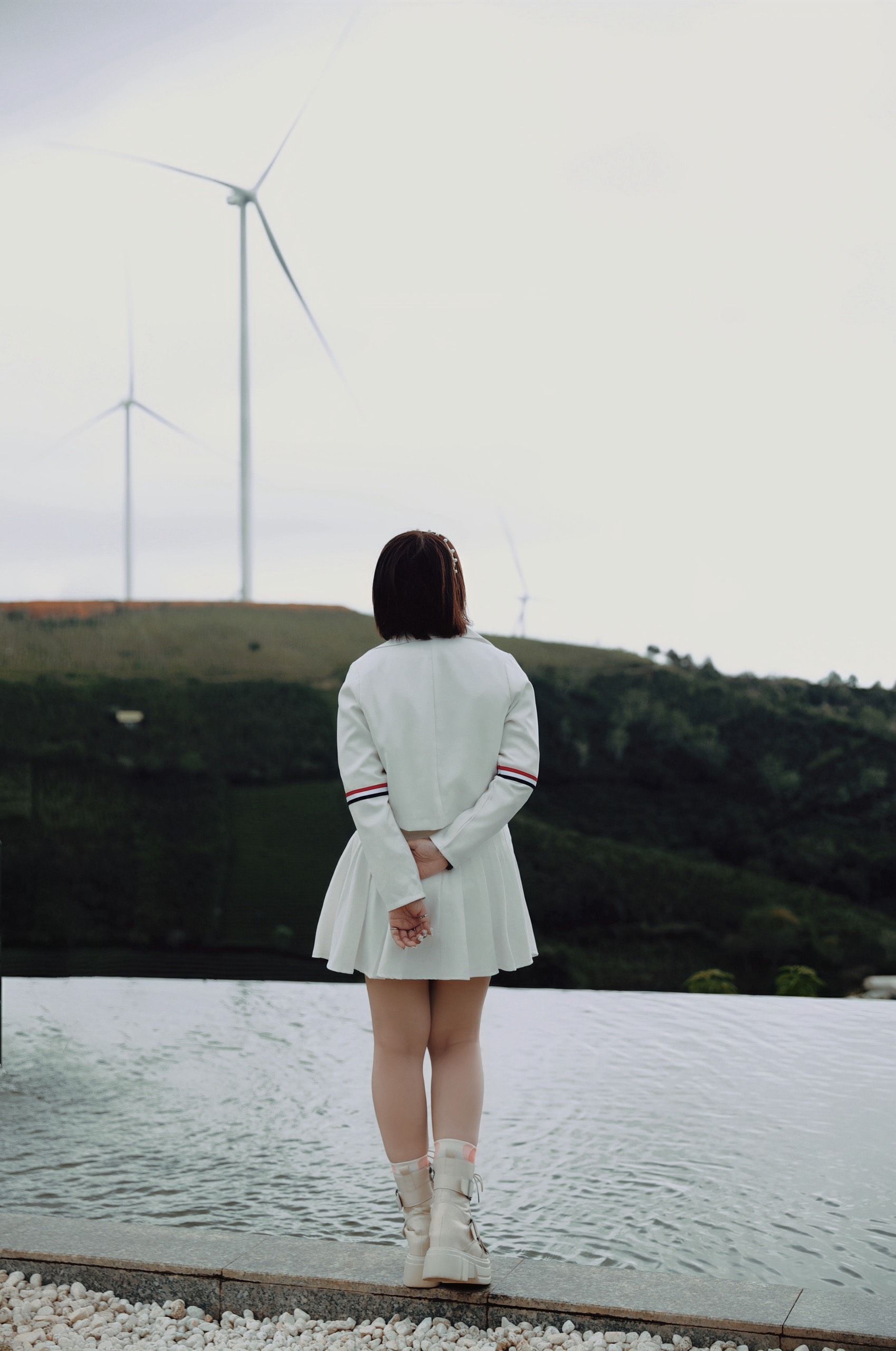Back view of a woman in a white outfit near windmills, symbolizing solitude and contemplation.