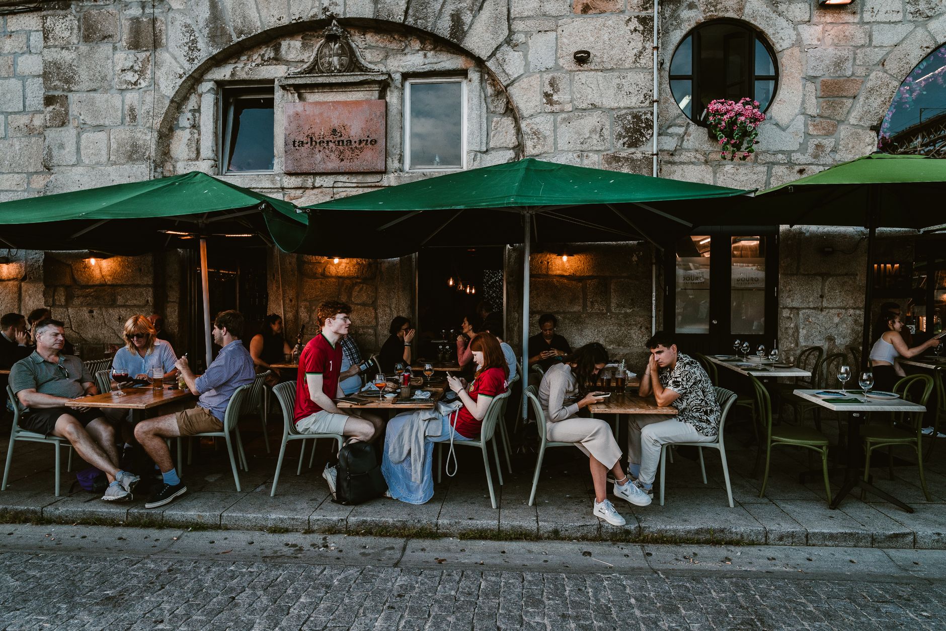 People enjoying outdoor dining at a historic café in Porto, Portugal. Cobblestone street adds charm.
