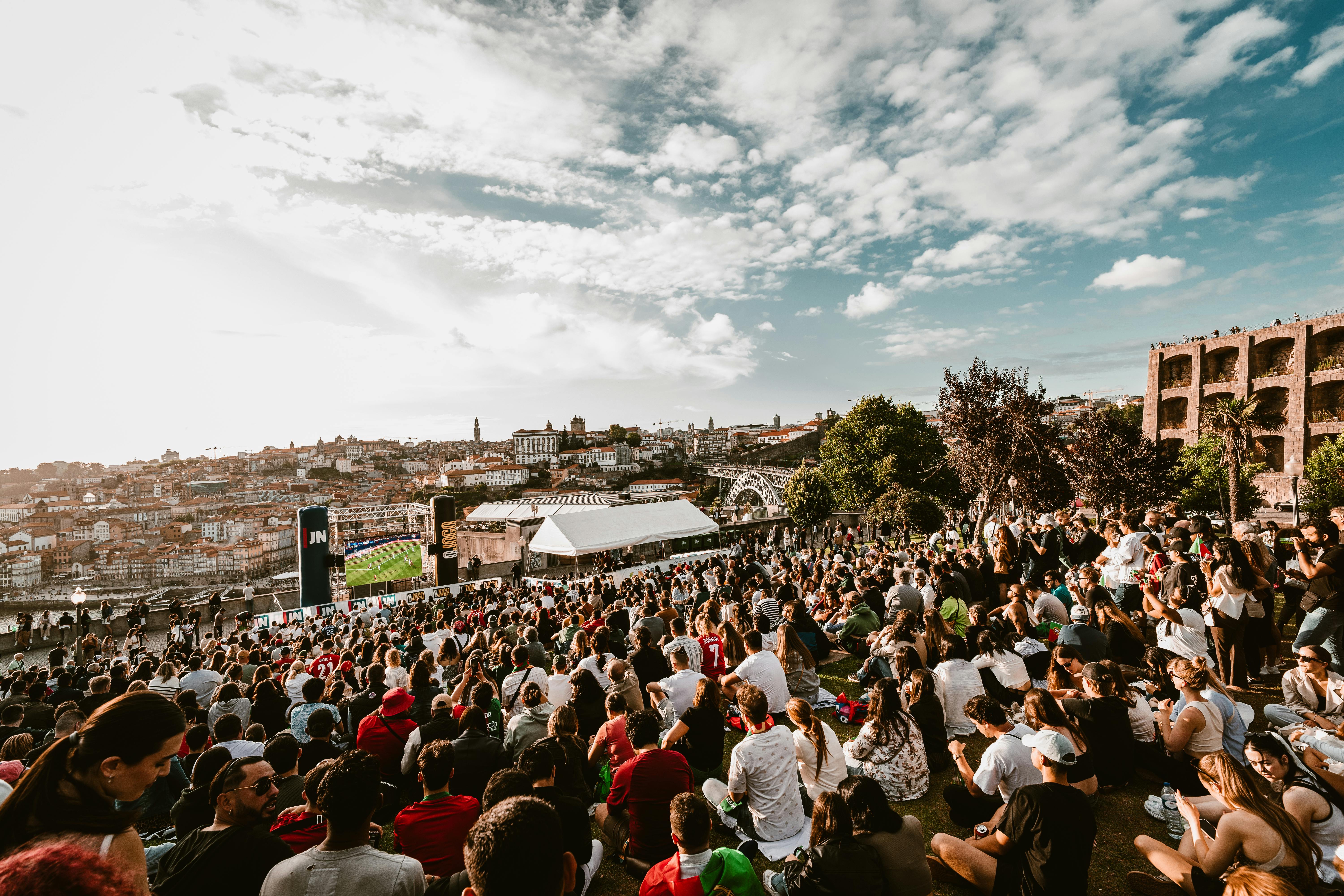 A large crowd gathers in Porto, Portugal, watching a soccer match with the cityscape as a backdrop.