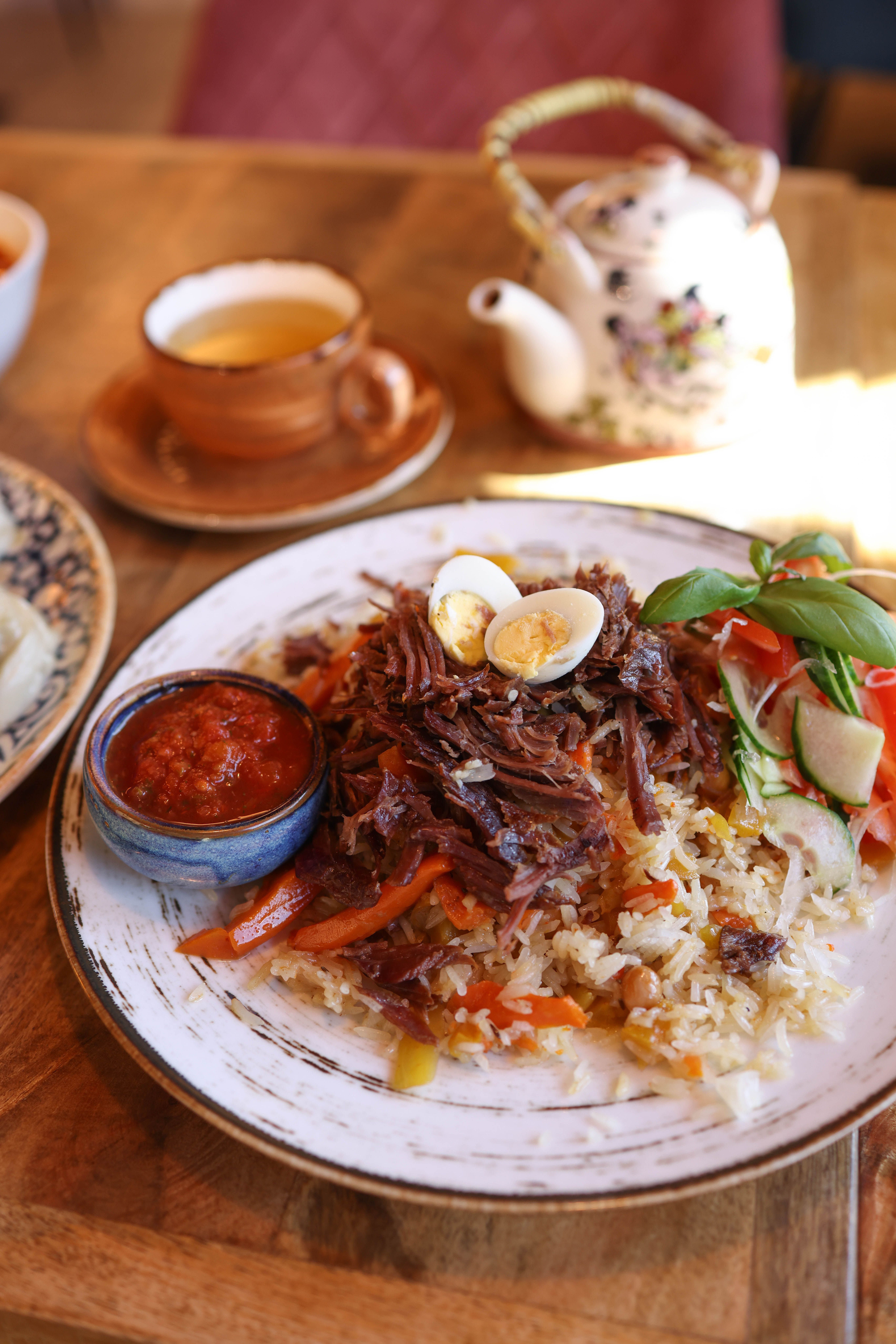 A delectable meal featuring shredded beef, rice, vegetables, and quail eggs, served with a side of spicy sauce.